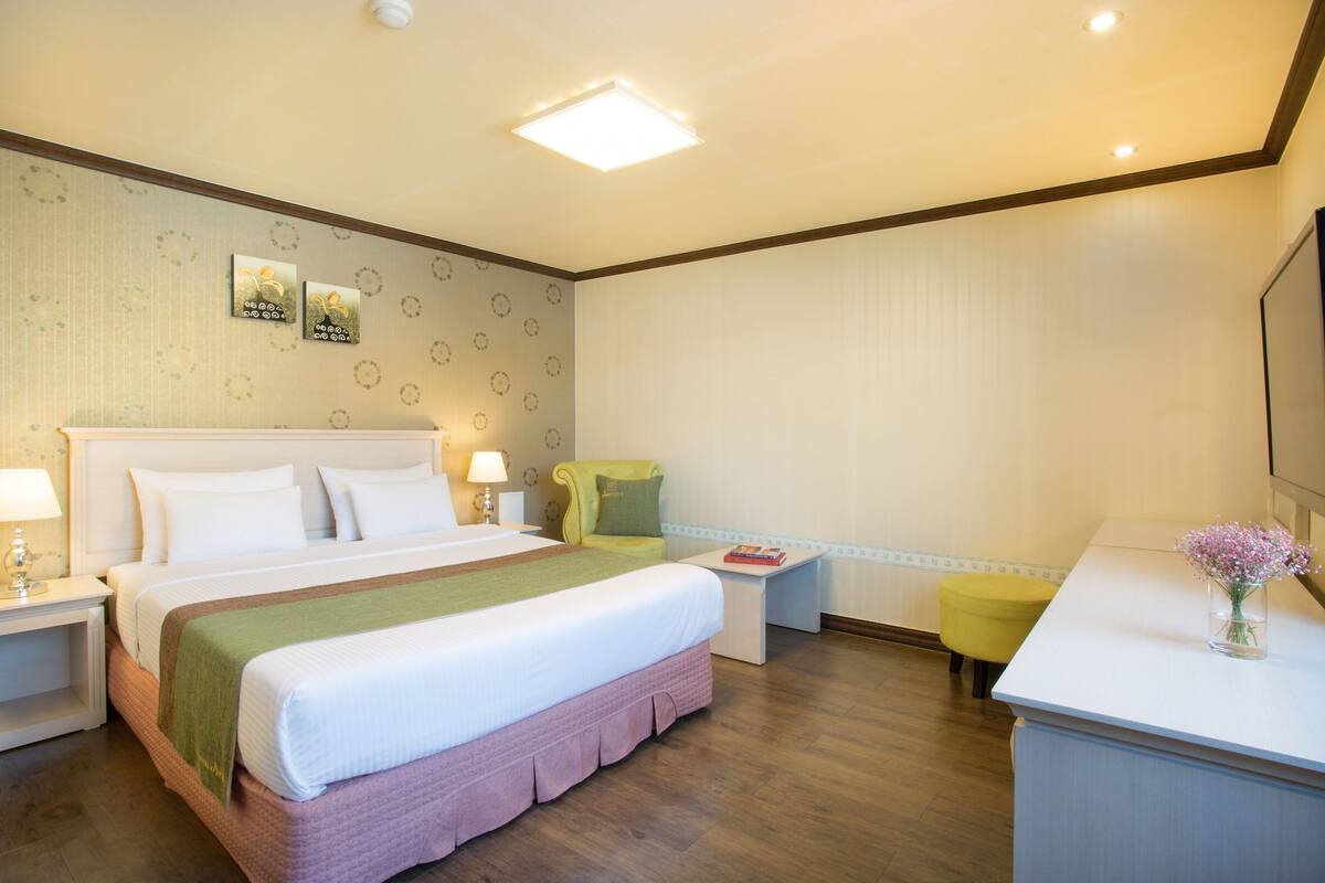 A hotel room with a large bed, bedside tables, a chair, a desk, and a mirror.
