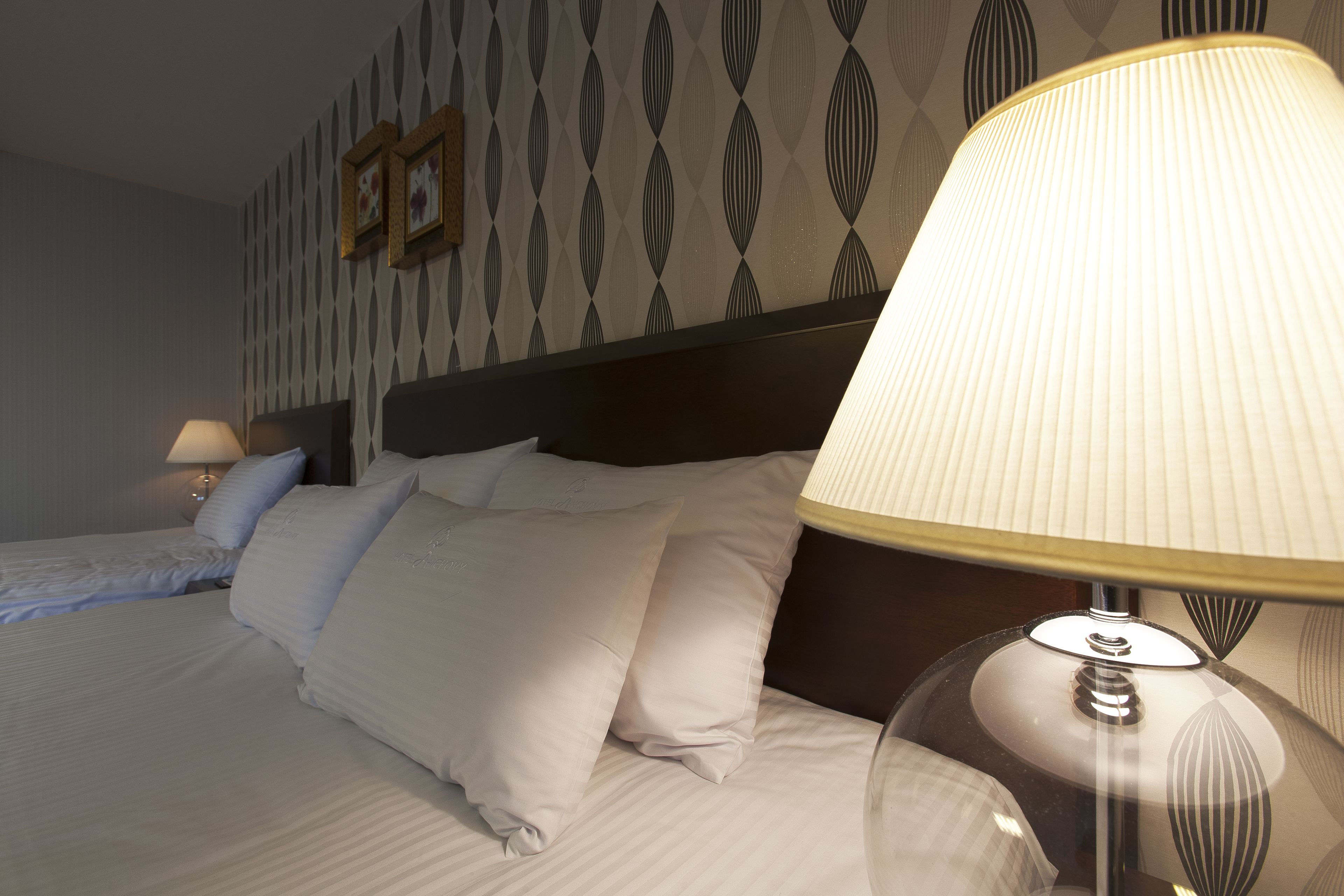 Quarto de hotel com duas camas, cabeceira e abajur.
