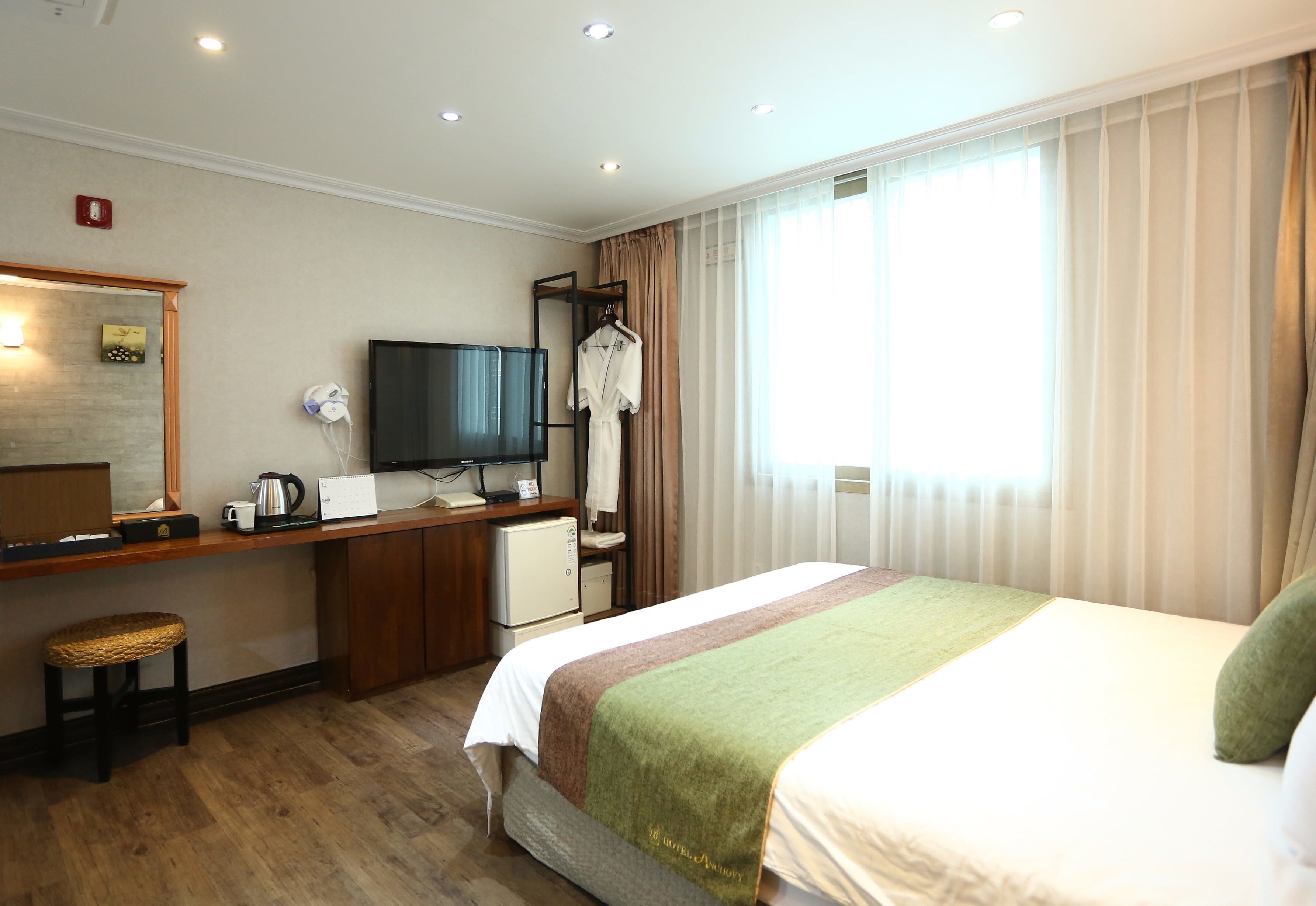 Una habitación de hotel con cama, escritorio con computadora, televisor y ventana con cortinas.