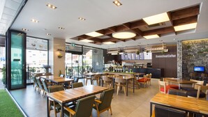 A modern cafe interior with wooden tables and chairs, a bar area, and a menu display. - Tongyeong Anchovy tourist Hotel (Tongyeong)