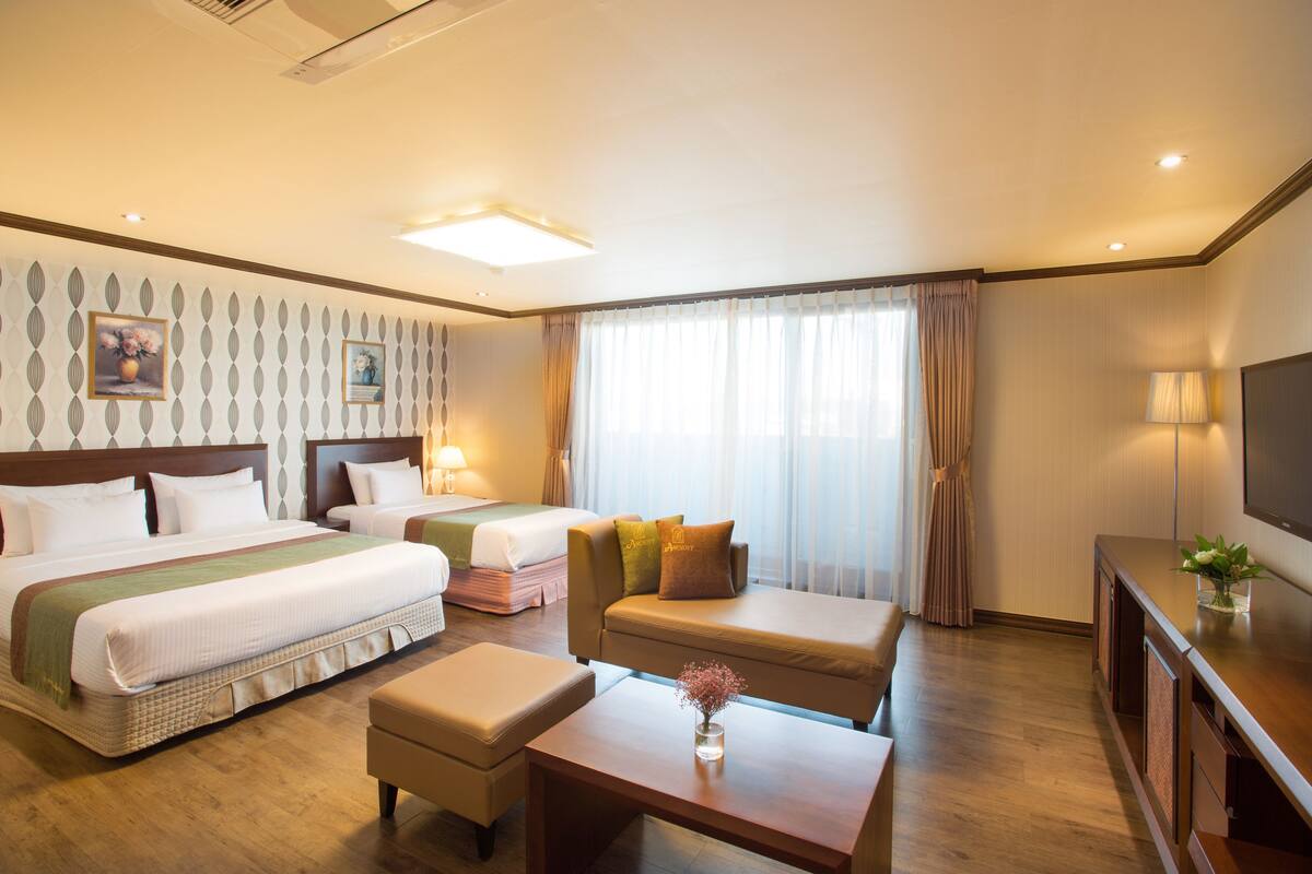 A hotel room with two beds, a sofa, a coffee table, and a TV.