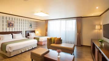 Habitación de hotel con dos camas, un sofá, una mesa de centro y un televisor.