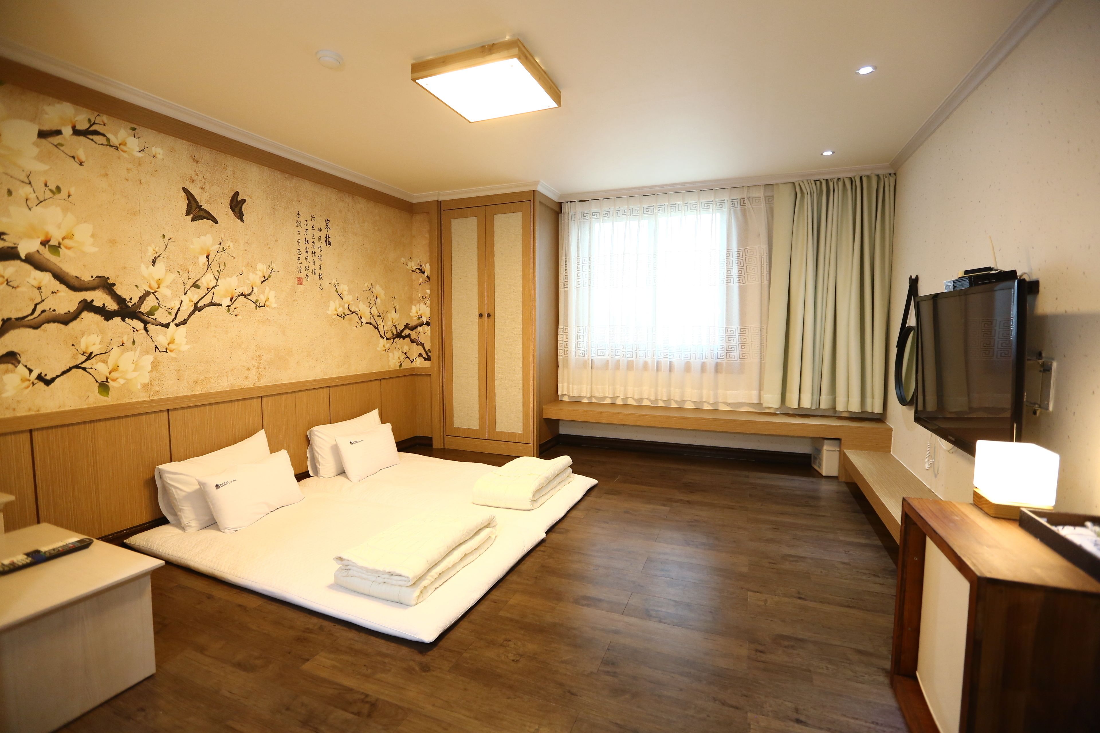 Ein Hotelzimmer mit einem großen Bett, einem Nachttisch, einem Fernseher und einem Fenster mit Vorhängen.