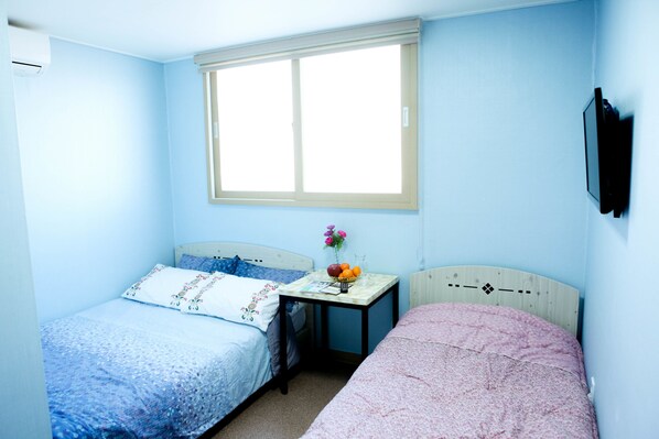 A bedroom with two beds, a window, a bedside table with a vase of flowers, and a wall-mounted TV. - WELL PLUS BNB Guest House (Seoul)