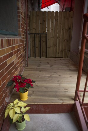 A wooden deck with a brick wall on one side and a wooden fence in the background. There are two potted plants on the deck. - WELL PLUS BNB Guest House (Seoul)