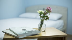 A wooden bedside table with a vase containing flowers and a book. - WELL PLUS BNB Guest House (Seoul)