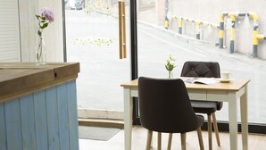 A cafe with a wooden counter, a vase with flowers, a table with a chair, and a view of the street outside. - WELL PLUS BNB Guest House (Seoul)