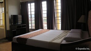 A hotel room with a bed, a television, a desk, and a window with curtains.