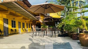 Um edifício amarelo com área de estar coberta ao ar livre, plantas em vasos e uma escadaria que leva a um andar superior.