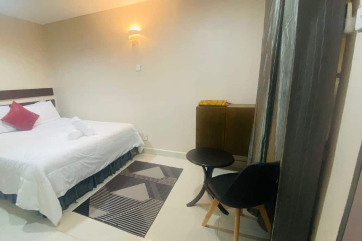 Une chambre d’hôtel avec un lit, une petite table ronde, une chaise et un luminaire fixé au mur.