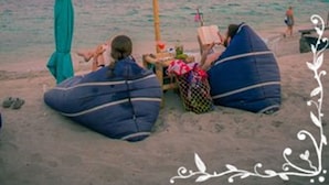 Une scène de plage avec des guirlandes lumineuses, des fauteuils en forme de sac et un poteau en bambou.