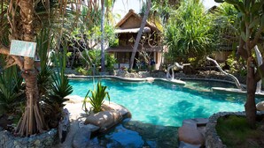 Une piscine entourée d’une végétation tropicale et bordée d’une structure à toit de chaume.