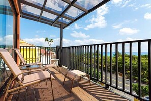 A balcony with wooden flooring, metal railings, and two lounge chairs.