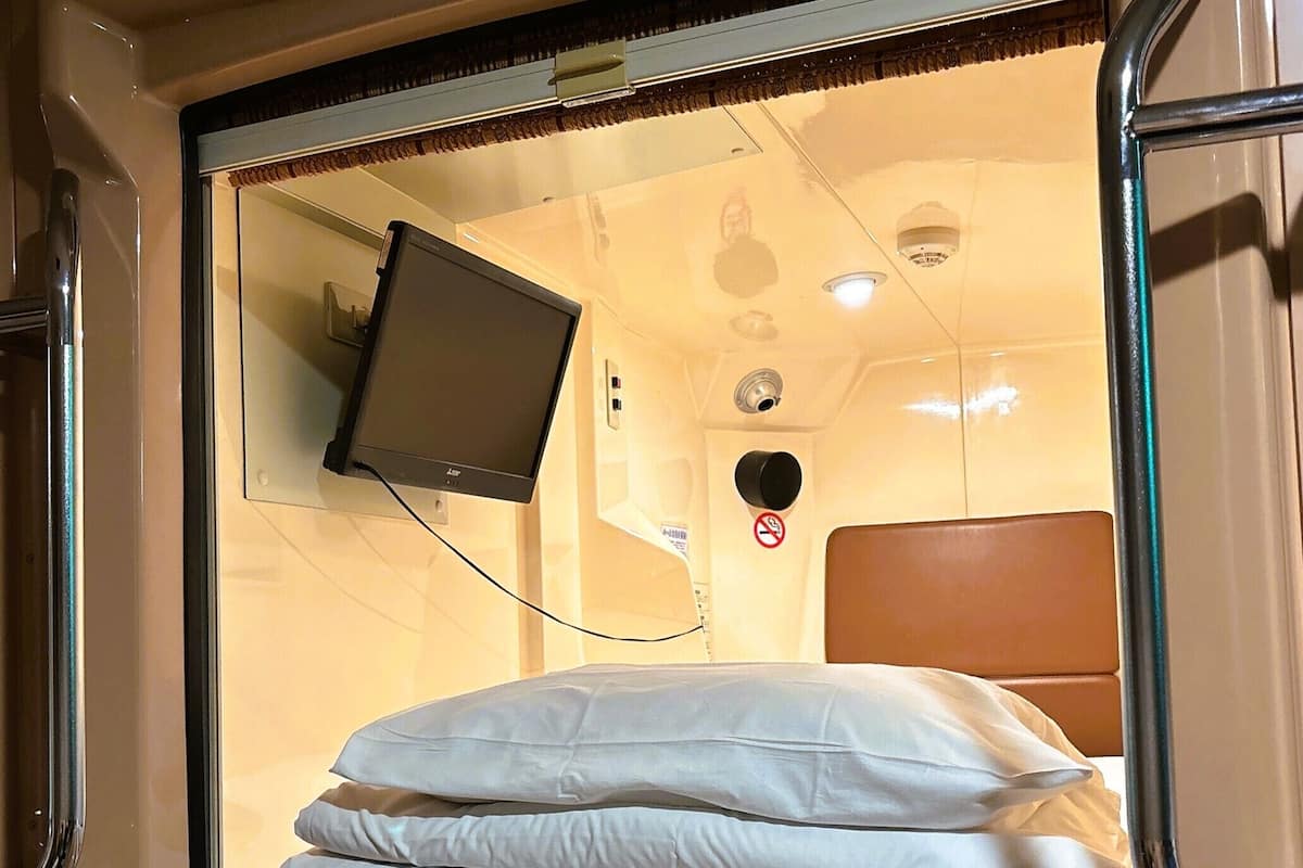 A hotel room with a bed, a television mounted on the wall, and a window.