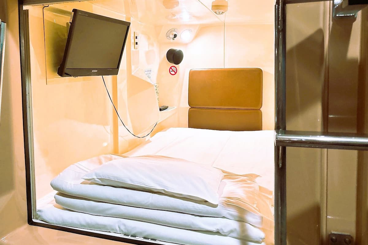 A compact, single-bed room with a built-in television, a headboard, and a window.
