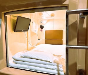A compact, single-bed room with a built-in television, a headboard, and a window.