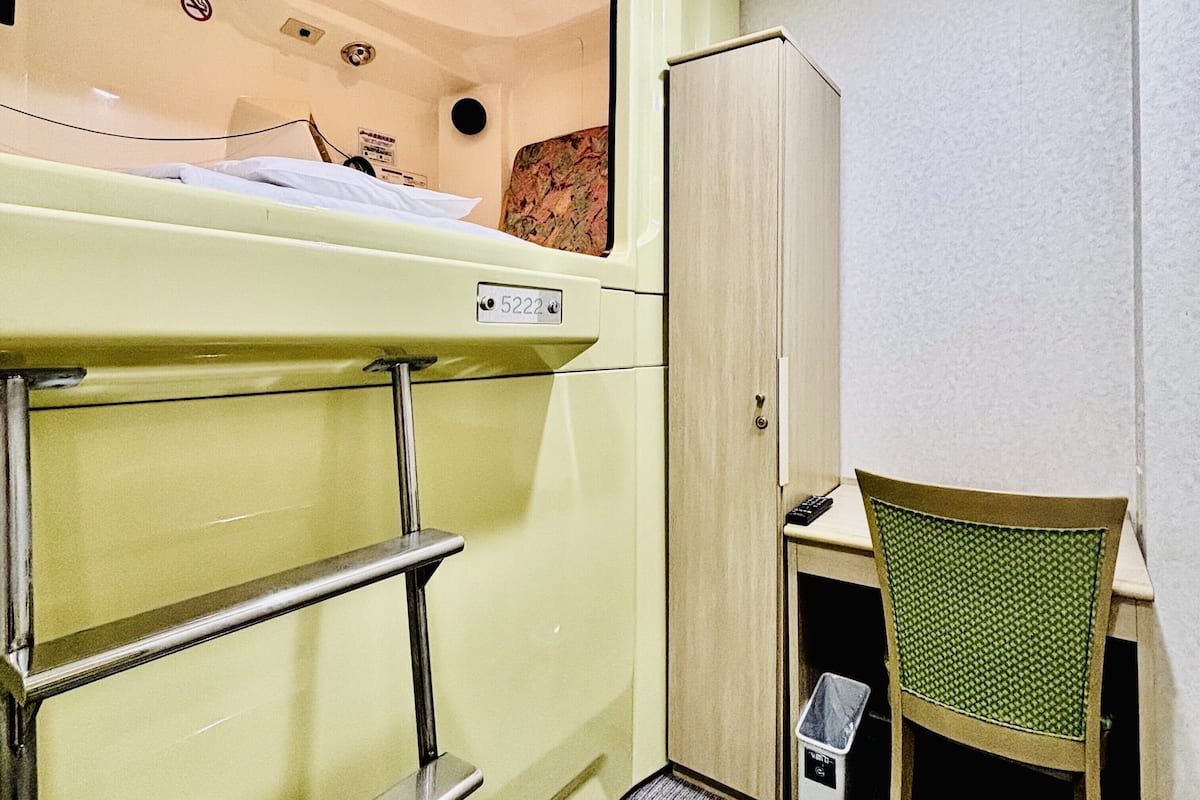 A small room with a bunk bed, a cabinet, a chair, and a trash bin.