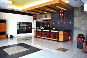 A hotel reception area with a modern design, featuring a reception desk, a digital screen, and a seating area with a small plant. - Subic Bay Venezia Hotel (Olongapo)