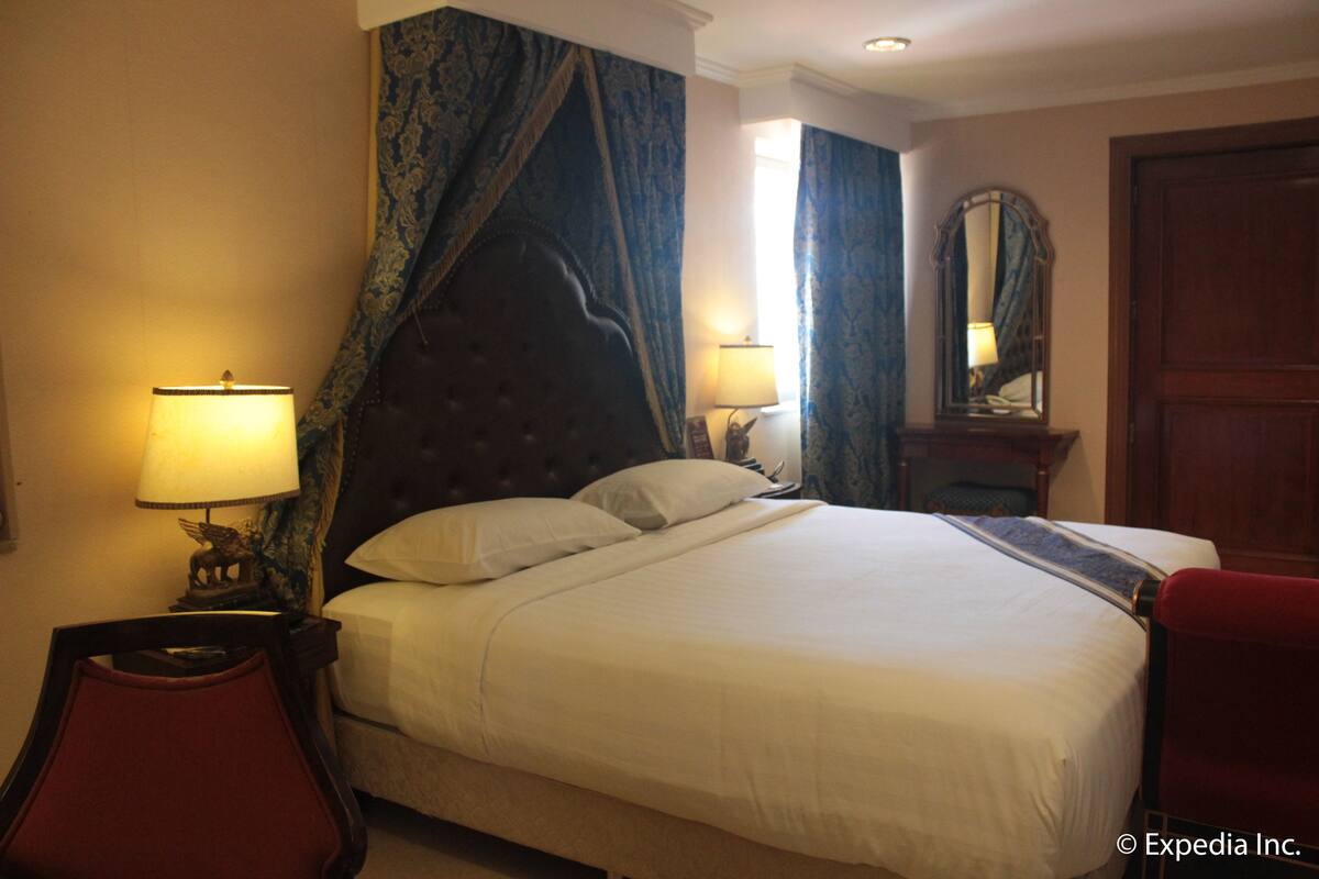 A hotel room with a large bed, two bedside lamps, a mirror, and a red chair.