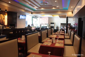 A restaurant with booths and tables, a TV screen, and a patterned wall. - Subic Bay Venezia Hotel (Olongapo)