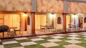 A courtyard with checkered flooring, outdoor seating, and a building with columns and warm lighting.