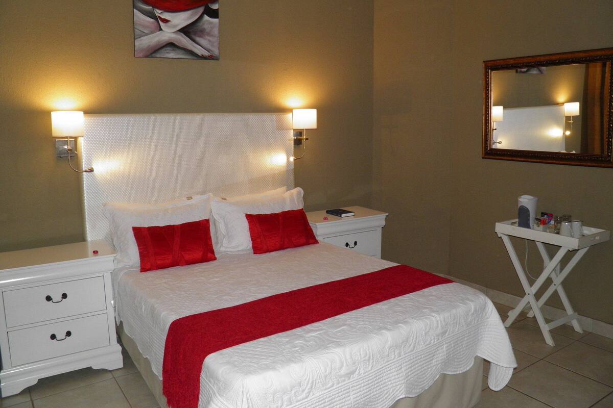 A hotel room with a large bed, white nightstands, a bedside table, a mirror, and a painting on the wall.