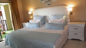 A bedroom with a large bed, two bedside tables, a nightstand, and a balcony with a curtain.