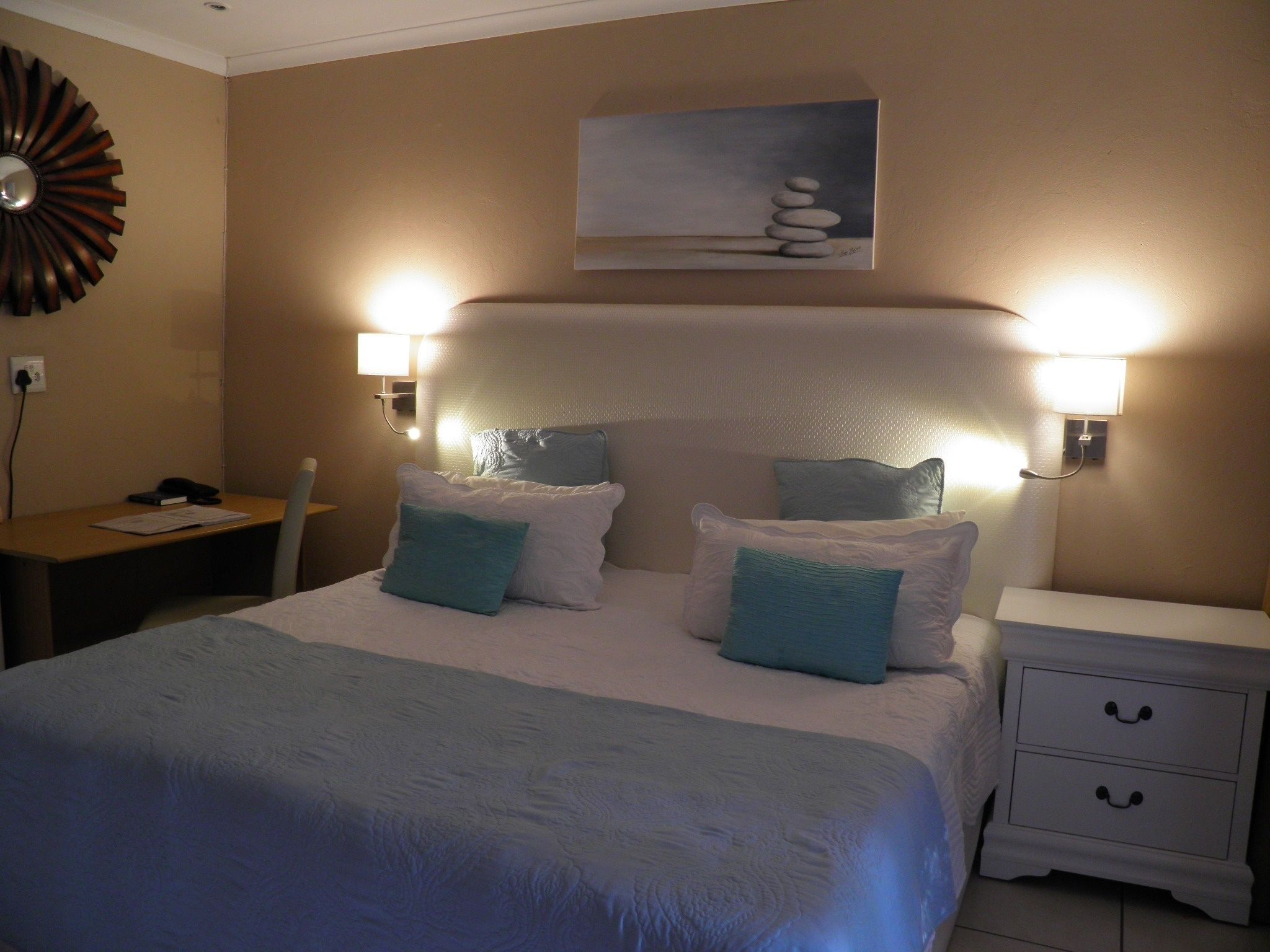 A hotel room with a bed, bedside tables, and a desk.