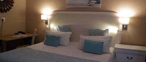 A hotel room with a bed, bedside tables, and a desk.