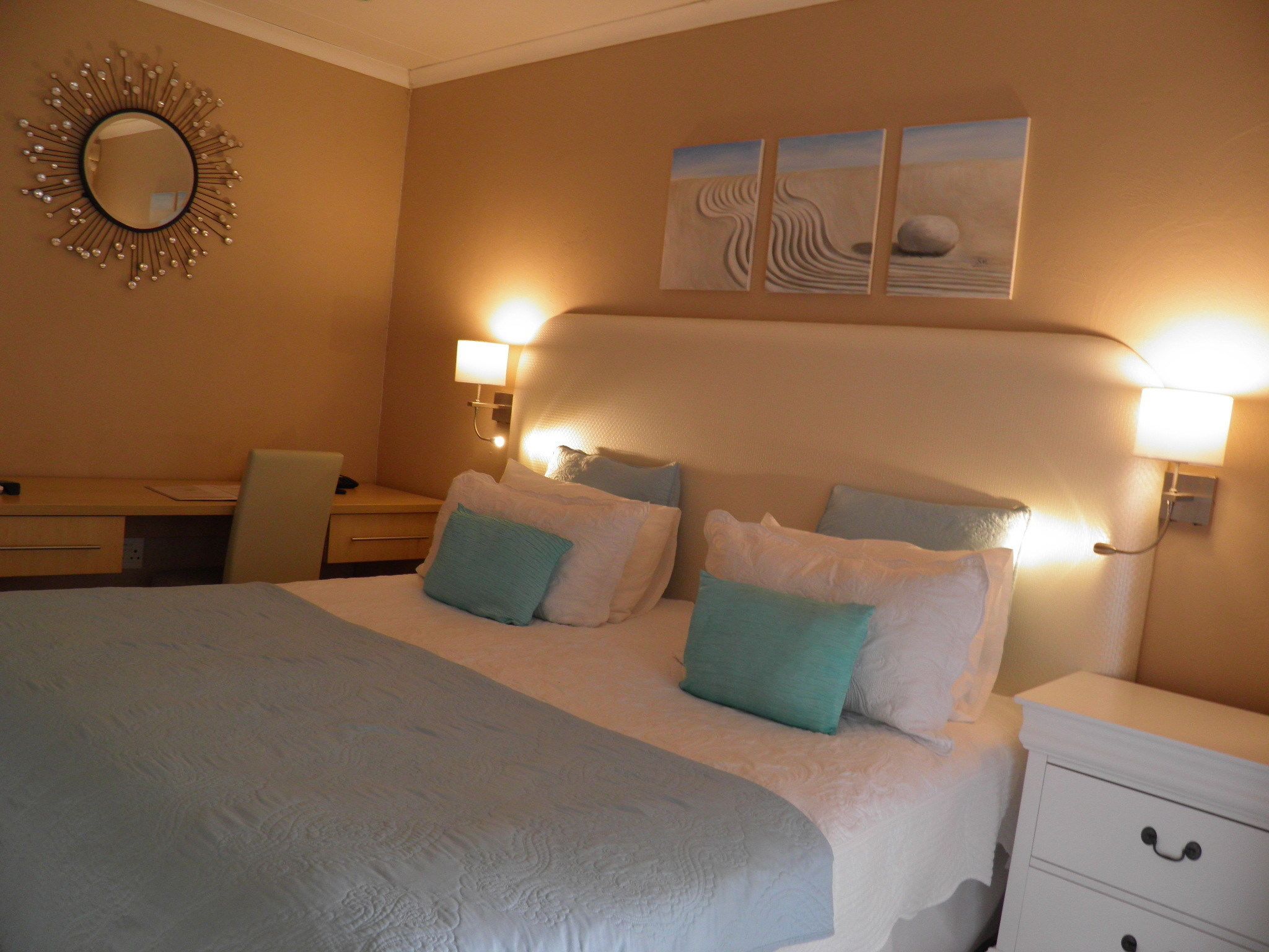 A hotel room with a large bed, two bedside tables, a desk, and a wall-mounted mirror.