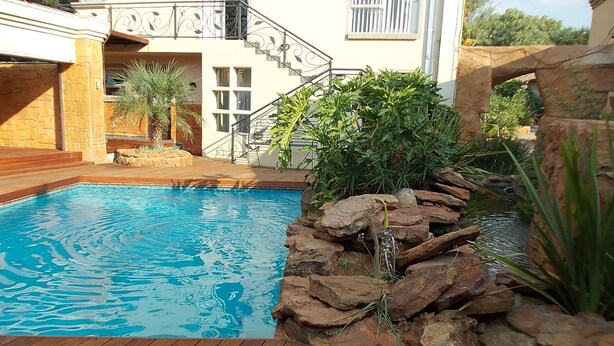 A swimming pool with a wooden deck, surrounded by a stone wall and plants.
