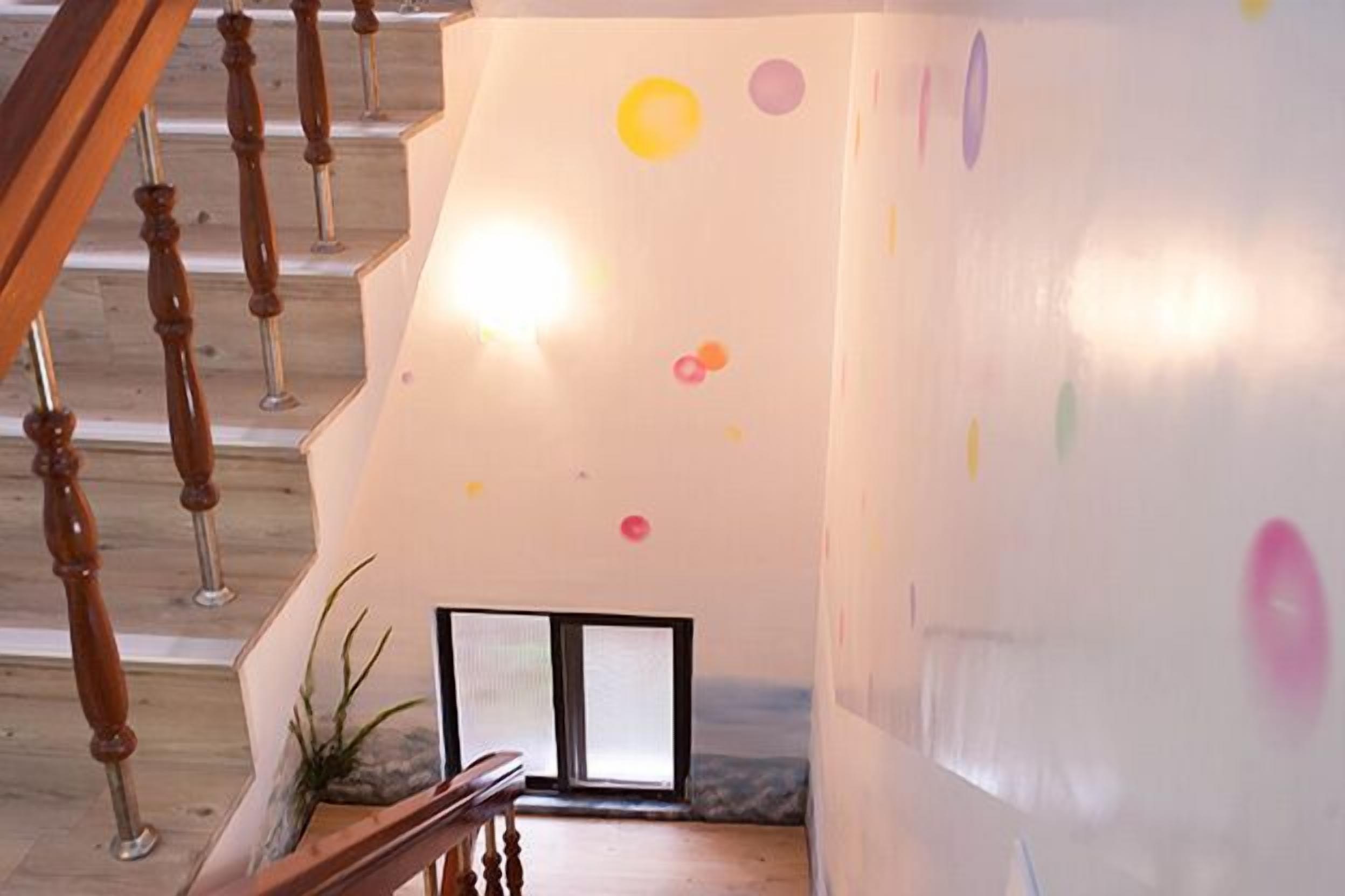 Una escalera con balaustres de madera, una puerta de vidrio al pie y una pared con decoraciones circulares coloridas.