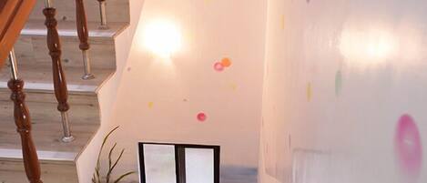 Una escalera con balaustres de madera, una puerta de vidrio al pie y una pared con decoraciones circulares coloridas.
