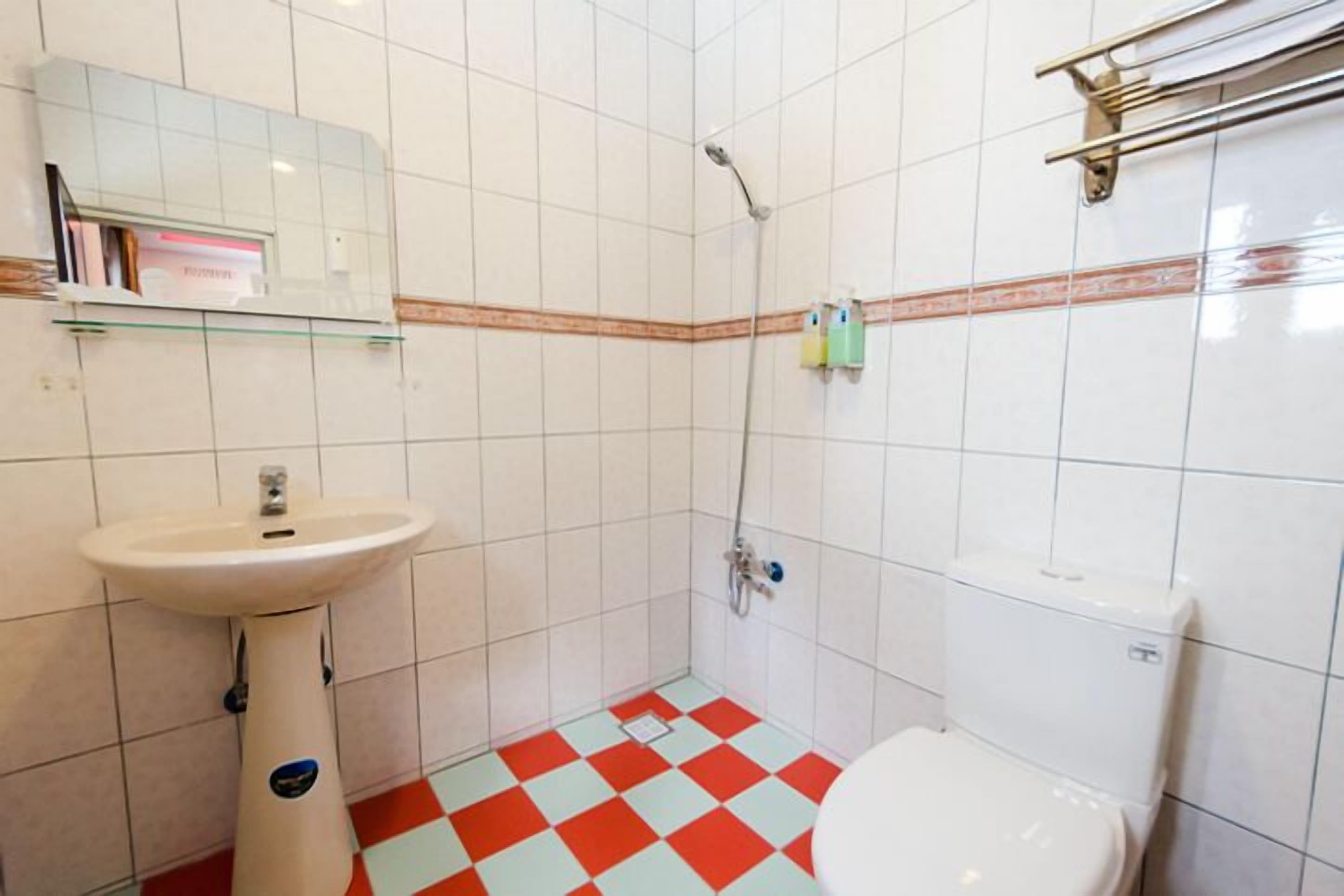 A bathroom with a white sink, toilet, and shower. The floor has a red and white checkered pattern.