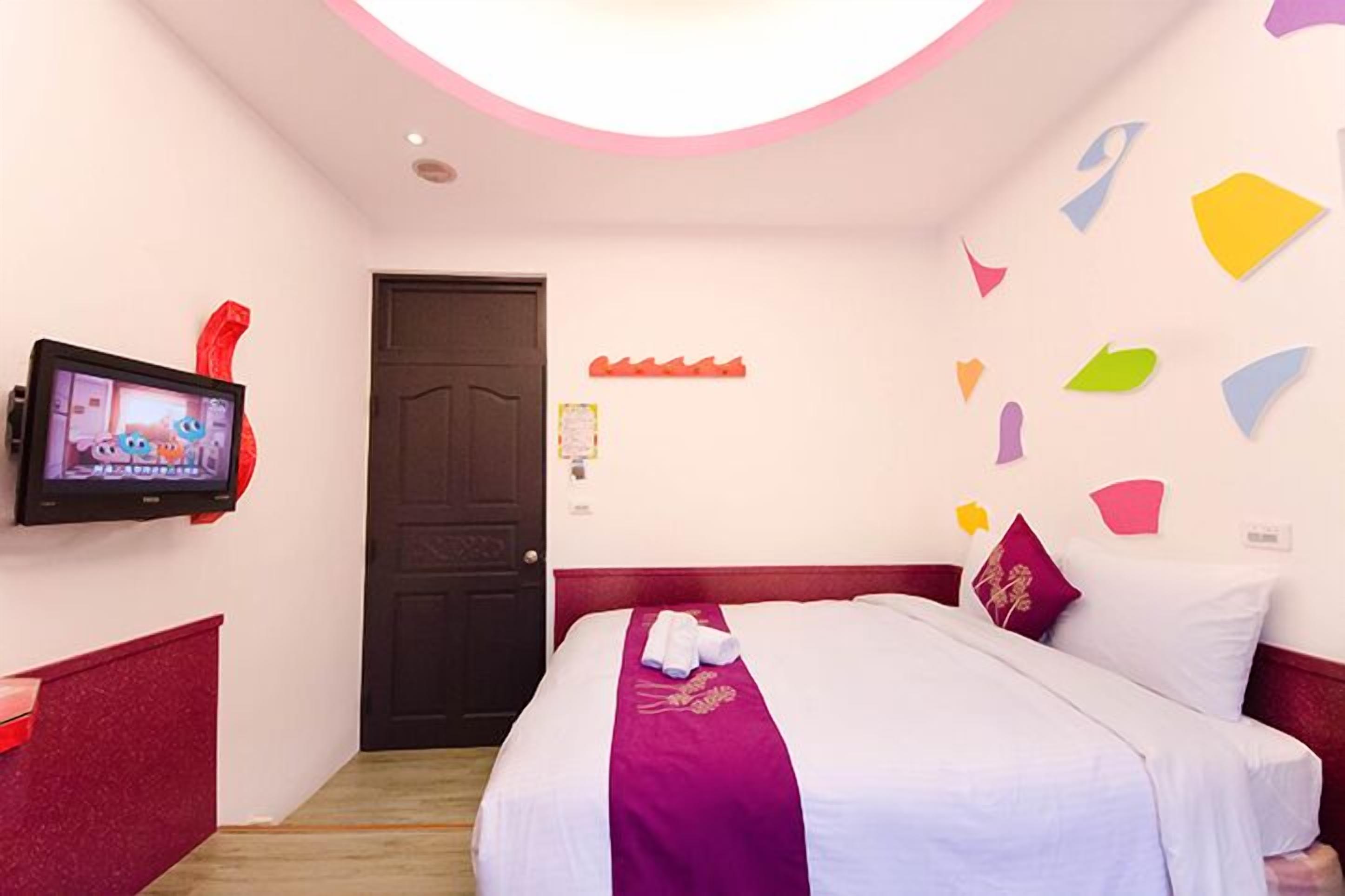 A hotel room with a bed, a TV on the wall, and a door.