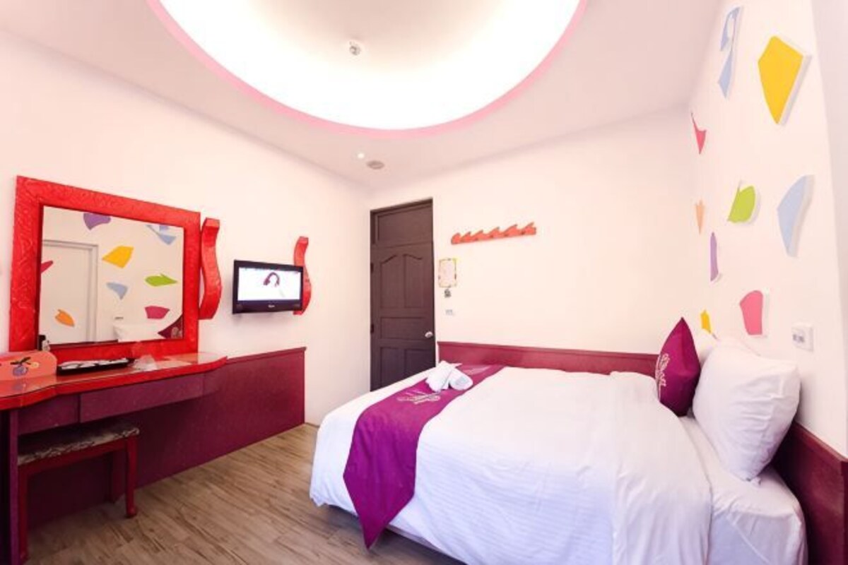 A bedroom with a bed, a desk, a mirror, a television, and a door.