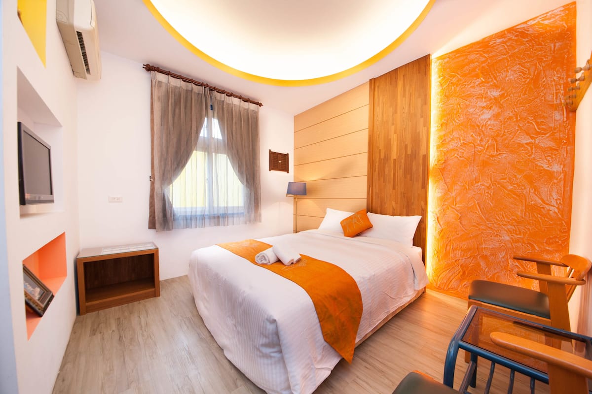 A modern hotel room with a large bed, a wooden headboard, a small desk, and a chair.