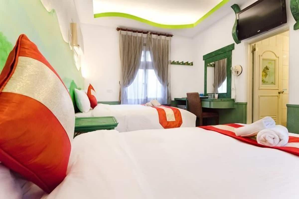 A hotel room with two beds, a desk, a chair, a mirror, and a door.
