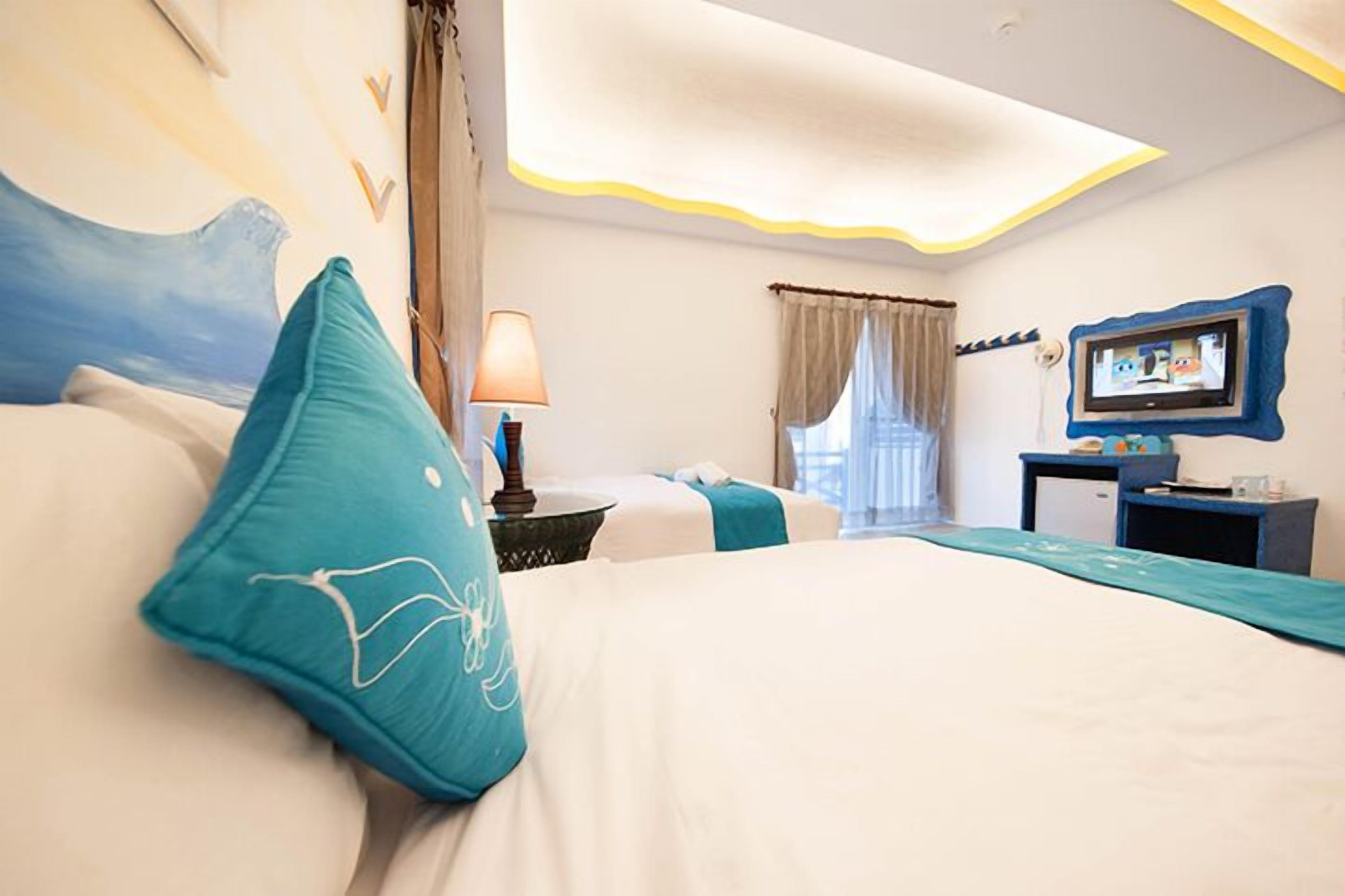 Habitación de hotel con cama, televisión, escritorio y ventana con cortinas.