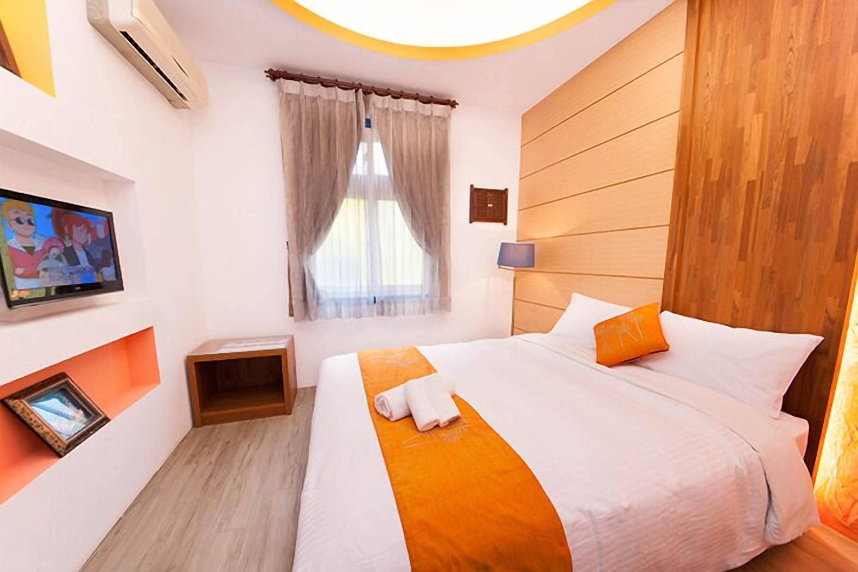 Une chambre d’hôtel avec un grand lit, un téléviseur fixé au mur, une petite table et une fenêtre avec des rideaux.