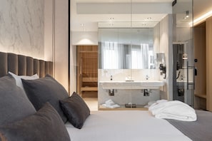 A modern hotel room with a large bed, a glass-enclosed bathroom, and a wooden closet.