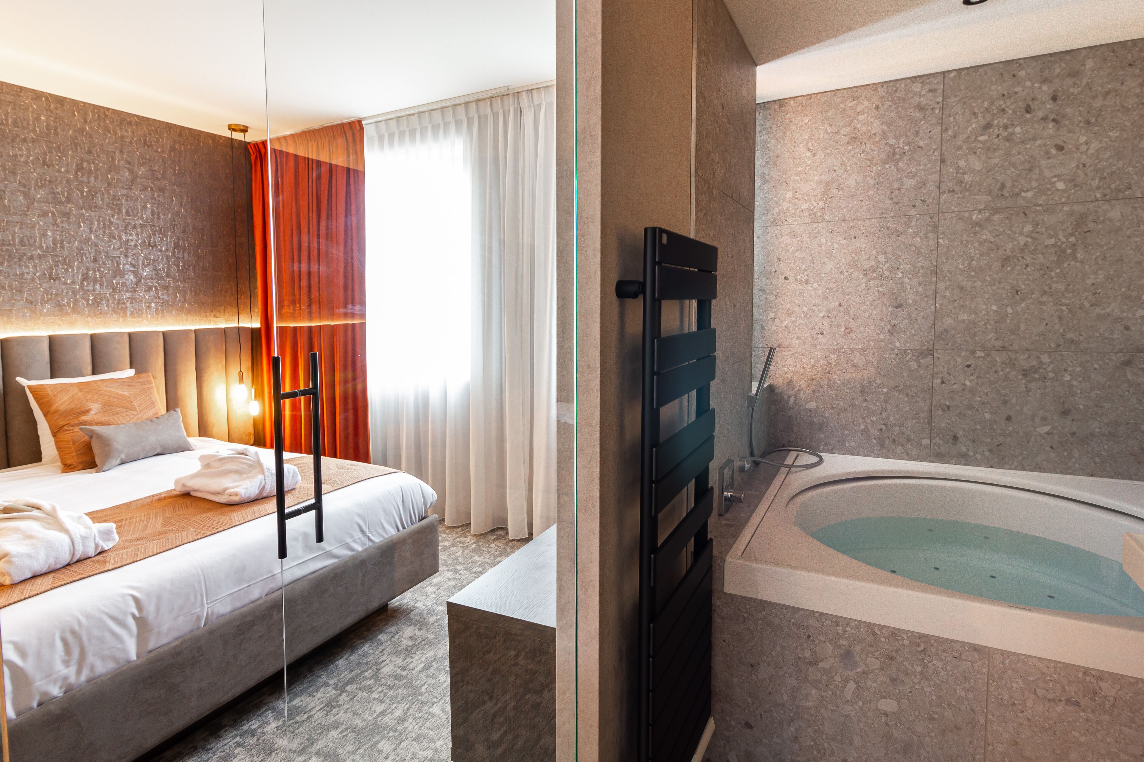 A modern hotel room with a large bed, a separate bathroom with a bathtub, and a view of the city.