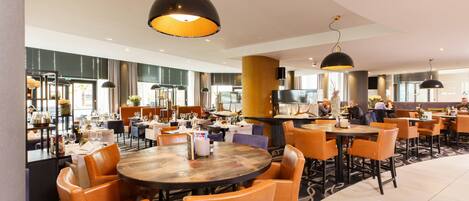 A spacious restaurant with round tables and orange chairs, large pendant lights, and a modern interior design.