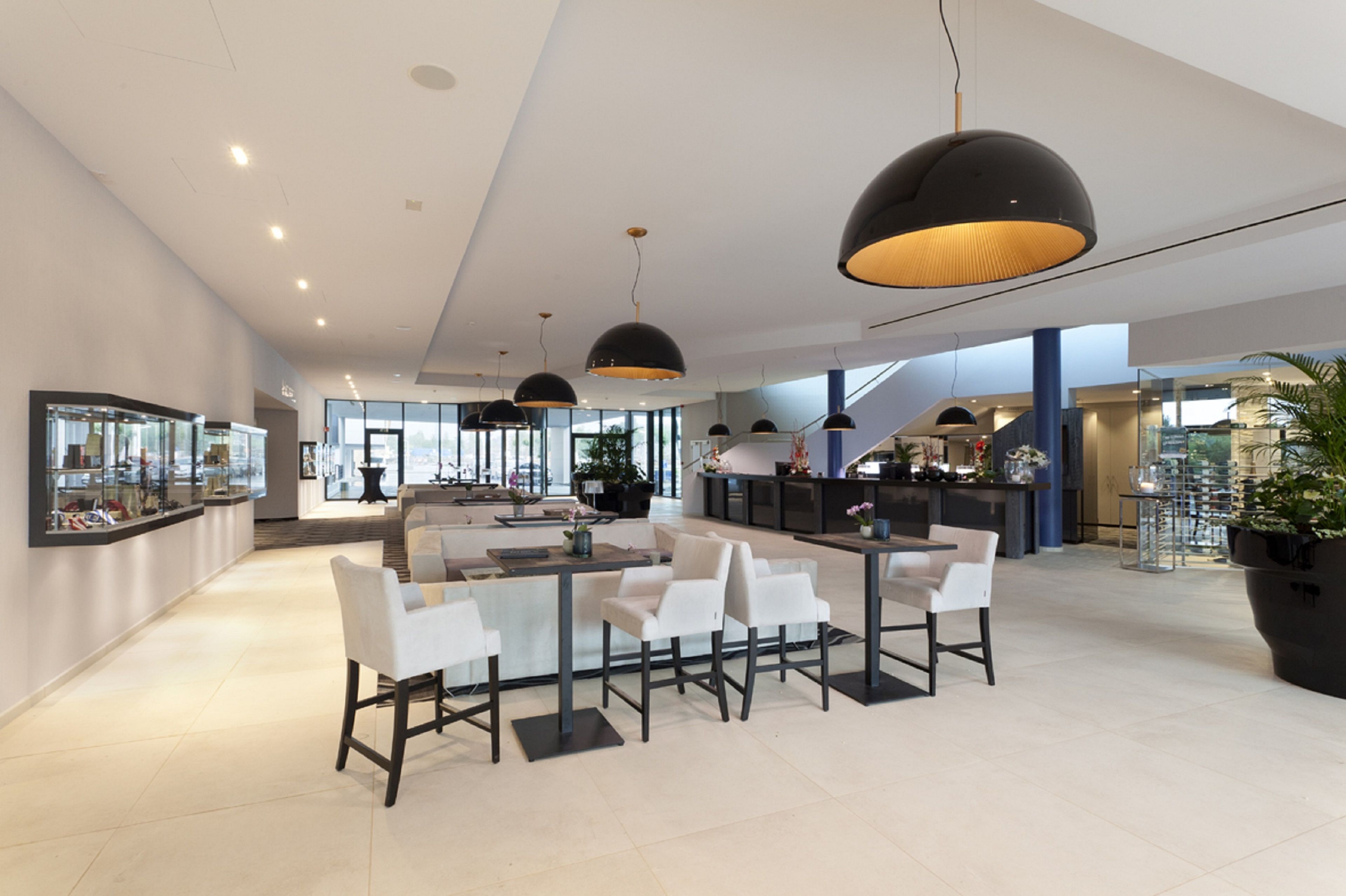 A spacious, modern lobby with a central seating area, large pendant lights, and a view of the kitchen area in the background.