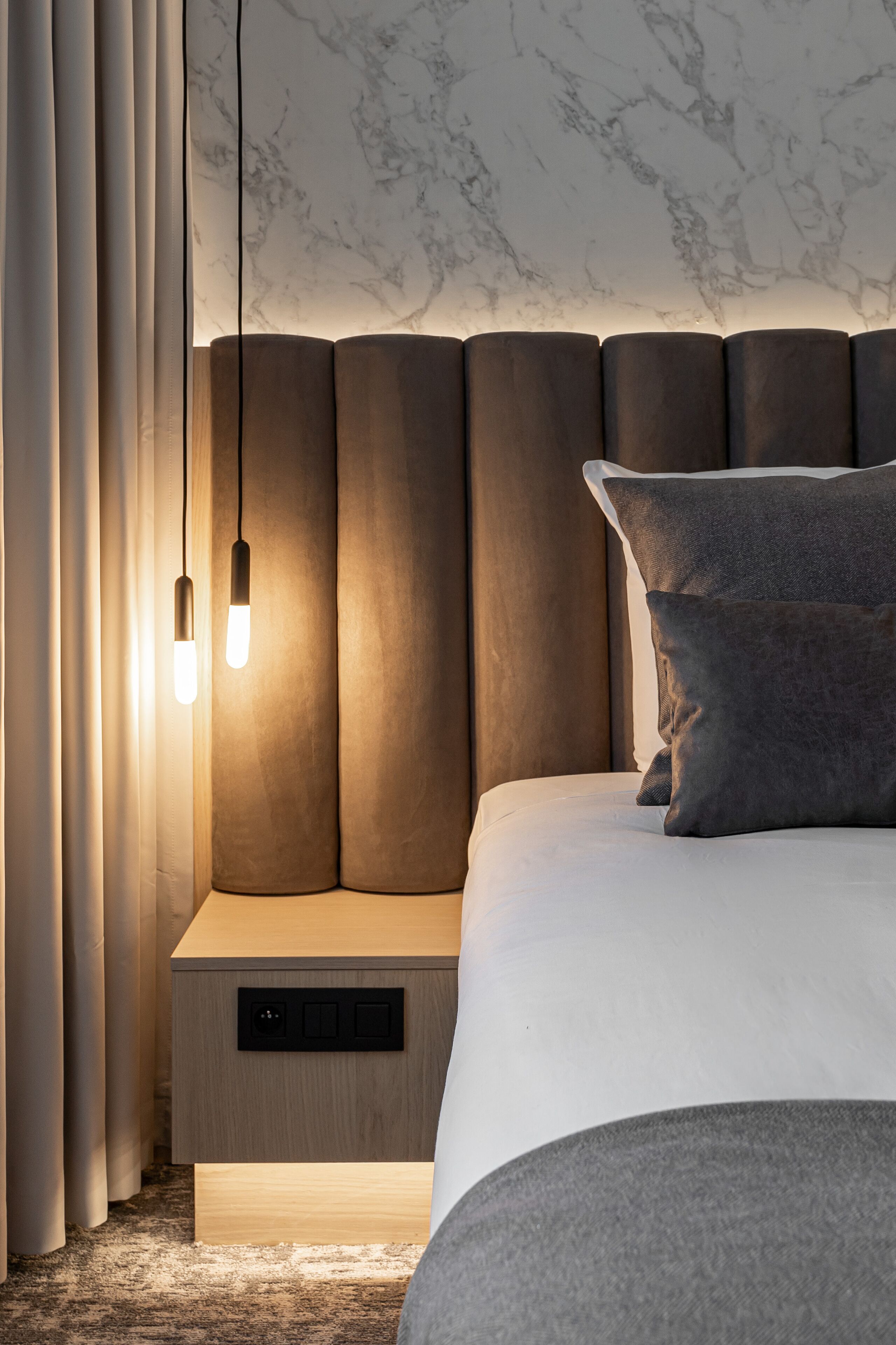 Un dormitorio moderno con cabecera de mármol, una mesita de noche con panel de control y una cama con almohada gris.