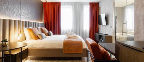 A modern hotel room with a large bed, a desk, a chair, a TV, and a large mirror.