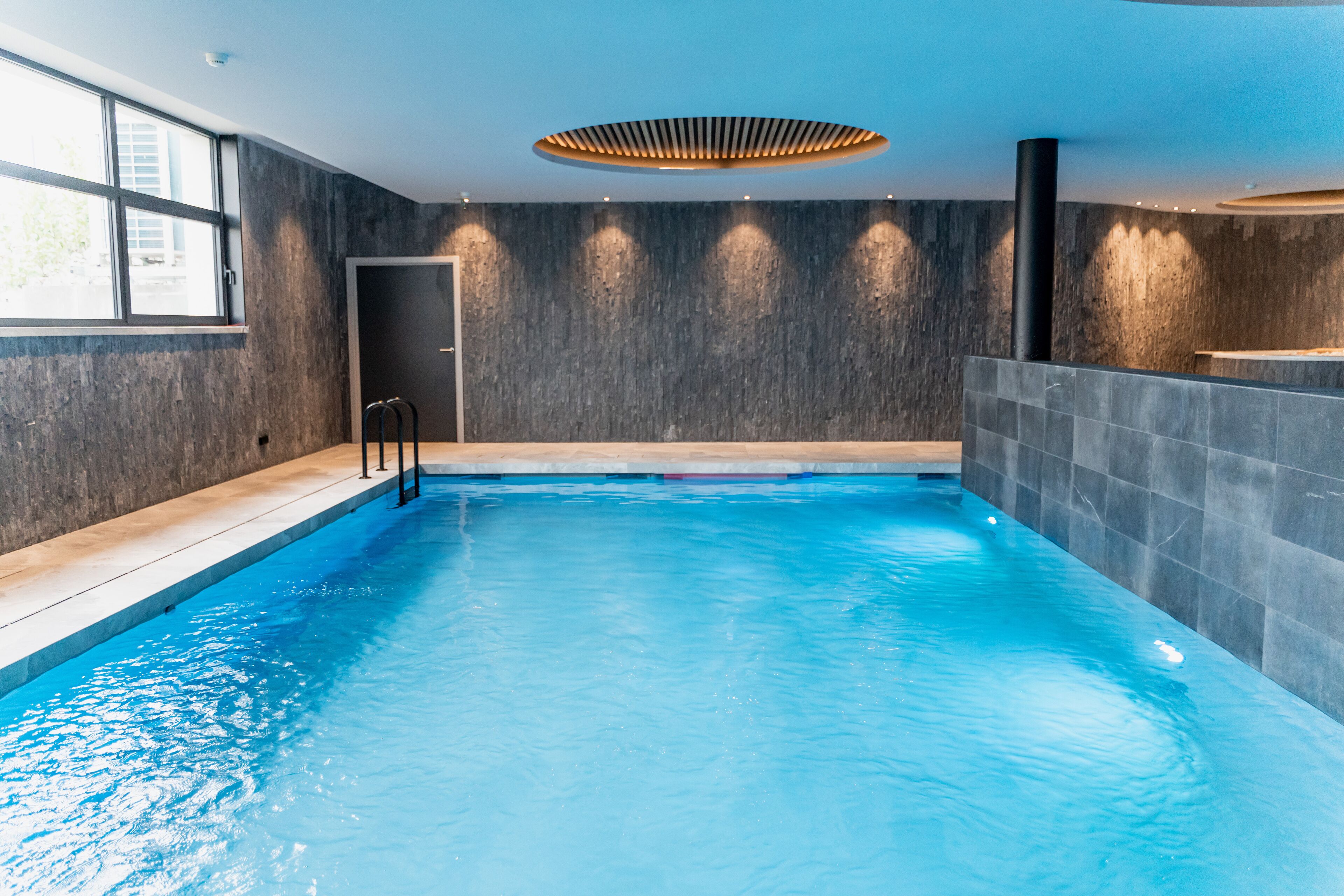 Una piscina interior moderna con vista despejada, techo de madera y un amplio ventanal a la izquierda.
