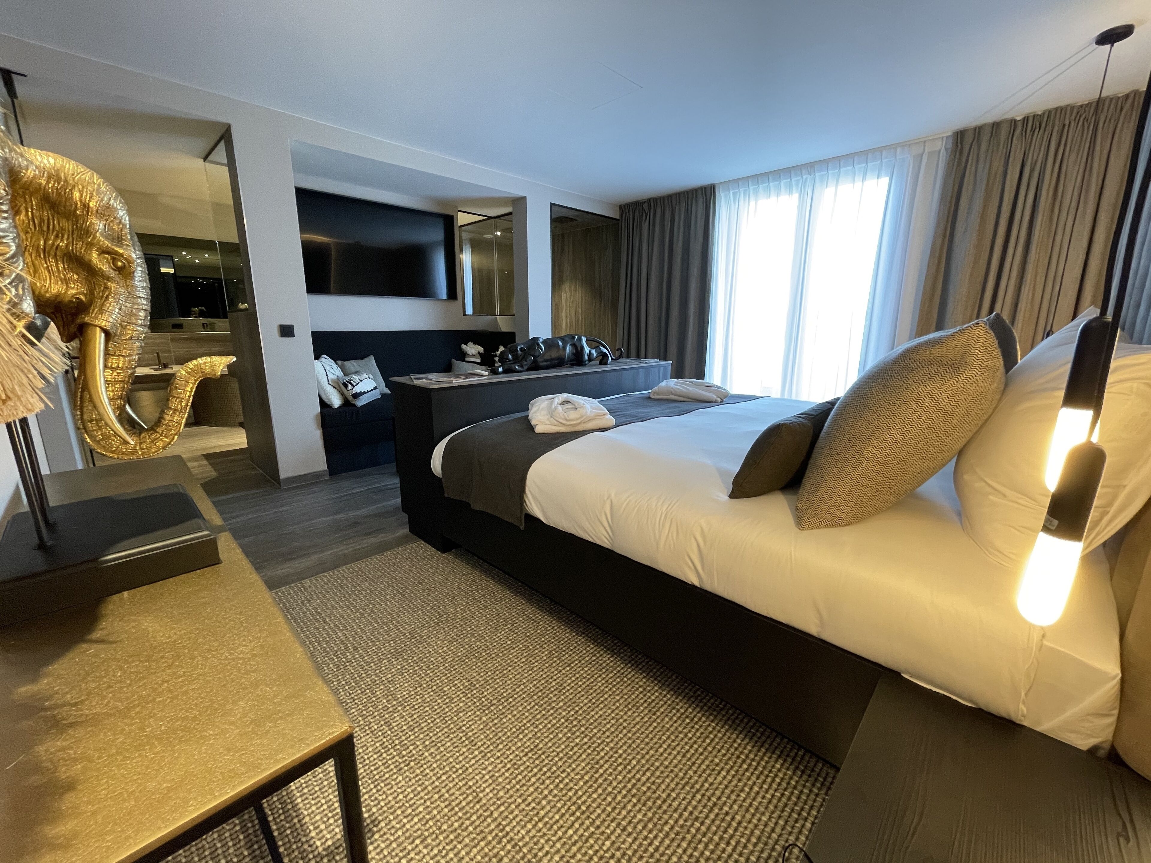 A modern hotel room with a large bed, a desk, a chair, and a television.