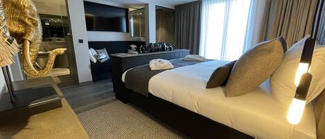A modern hotel room with a large bed, a desk, a chair, and a television.