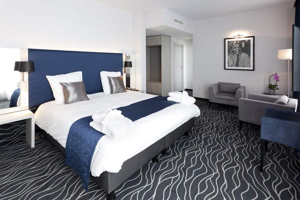 A modern hotel room with a large bed, a seating area, and a framed picture on the wall.